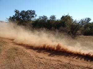 Dry field with dust cloud and trees in background